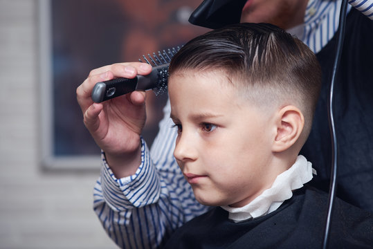 Barber is drying a hair to Caucasian boy in barbershop.