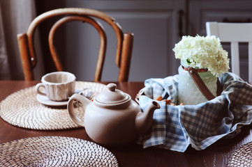 Obraz na płótnie Canvas cozy summer morning at rustic country house kitchen. Tea, cookies and bouquet of fresh flowers. Casual breakfast in grey and brown interior.