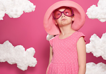 fashionable girl posing on a pink background with clouds, pink dress and hat