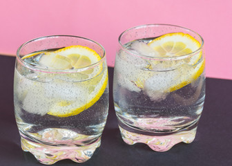 Two glasses of fresh cold water with lemon slices and ice on the pink pastel background. Healthy lifestyle.