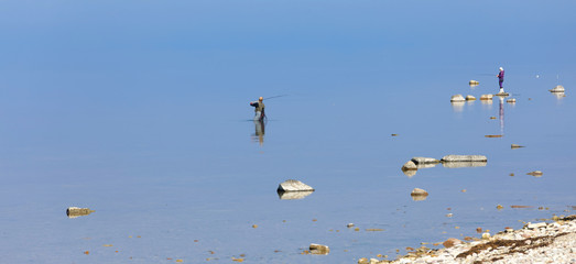 Obraz premium Two angler in the blue calm sea trying to catch trout at Aleklinta on the island Oland, Sweden
