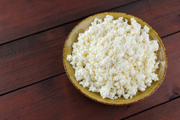 Cottage cheese on wooden boards, soft cheese on a yellow plate. Dairy product on a brown wooden background, healthy lifestyle. Copy space