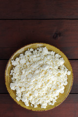 Cottage cheese on wooden boards, soft cheese on a yellow plate. Dairy product on a brown wooden background, healthy lifestyle. Copy space