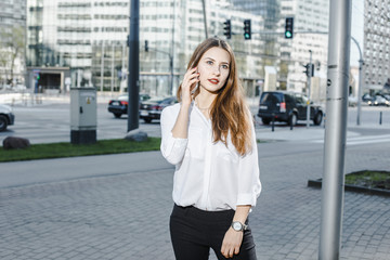 Fototapeta premium A business woman speaks through the phone. A good girl is sitting on the bench. A young woman in the city center.