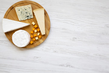 Tasting cheese on round bamboo board on a white wooden background. Food for wine, top view. Flat lay, from above. Copy space.