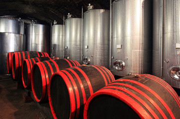 Wine barrels in wine cellar with modern fermentor tanks