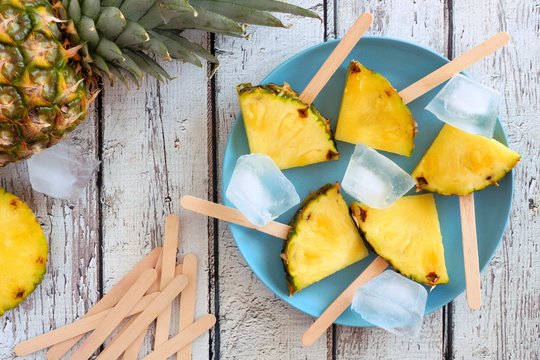 Pineapple slice popsicles. Top view table scene on a white wood background.