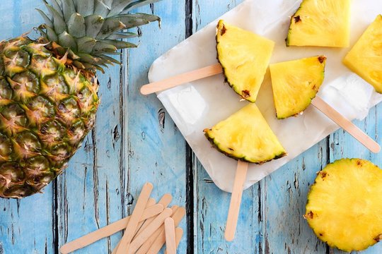 Pineapple slice popsicles. Top view table scene on a blue wood background. - Powered by Adobe
