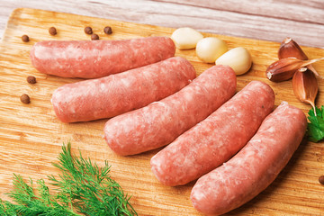 Sausages for grilling and garlic on a wooden cutting board