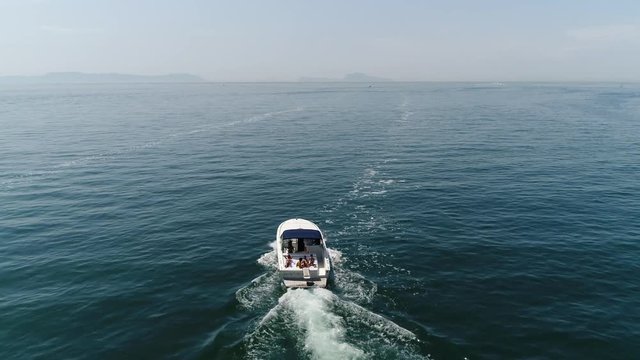 Aerial bird view footage flight behind motorboat cabin cruiser with sun tanning people on the stern of boat slow cruising over ocean water showing small waves from calm weather on beautiful summer day