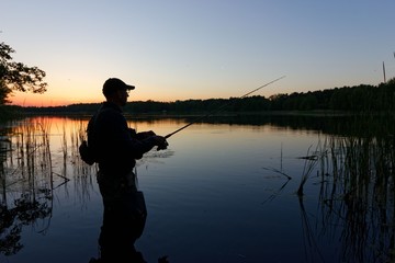 Silhouette of fisherman standing in the lake and catching the fish during sunset