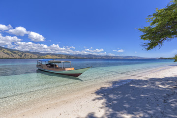 Fototapeta na wymiar A boat docked on a beautiful empty tropical indonesian Beach in the Seventeen Island National Park.
