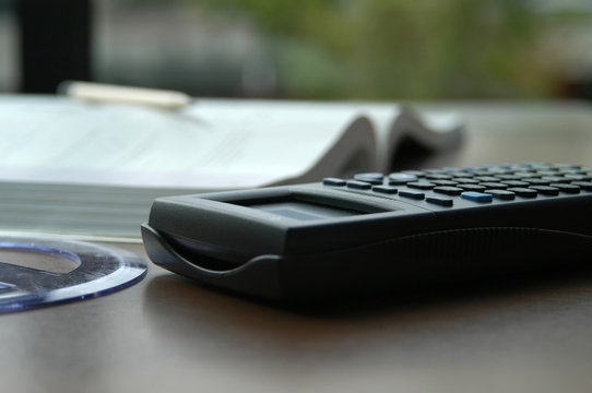 Math still life photos. Calculator, protractor, open book, and wooden pencil on a brown desk next to a window in a library at university. Studying math and doing homework at school.