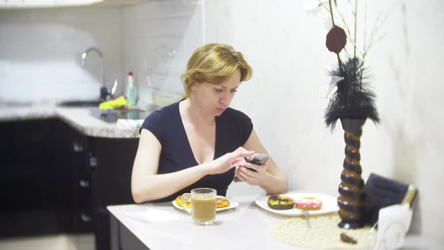 woman is eating pizza in the kitchen at home and using her smartphone, 4k, background blur