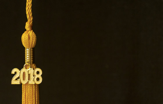 Class of 2018. Gold tassel drop graduation gown accessory and keepsake charm against a black background. Iconic symbol of a graduate's academic and life success.