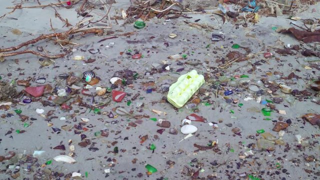 Tilt shot of the exposed ground of the polluted sandy beach with plastic and glass trash debris and dry grass. Environmental pollution problem concept. Glass Bottle Beach, Brooklyn, NY, USA.