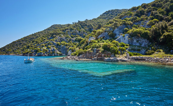 Sunken city of Kekova in bay of Uchagiz view from sea in Turkey with turqouise sea rocks and green bushes with remains of ancient city visible under water.