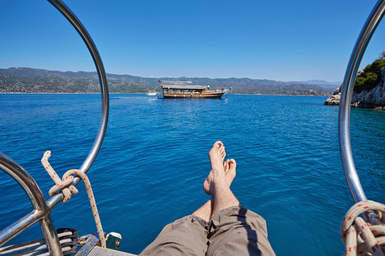feet of a young man on the nose of a yacht against the background of a beautiful clean sea