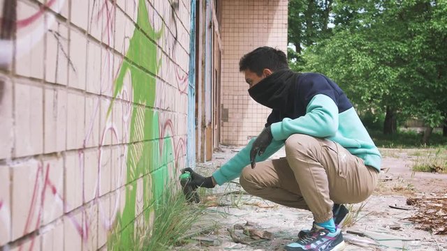 Young man graffiti artist painting on the wall, exterior