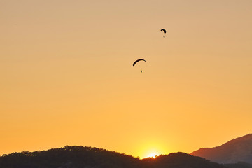 Paraglider silhouette flying over misty mountain valley in beautiful warm sunset colors - sport, active wallpapers full of freedom.