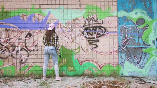 Young woman graffiti artist drawing on the wall, exterior