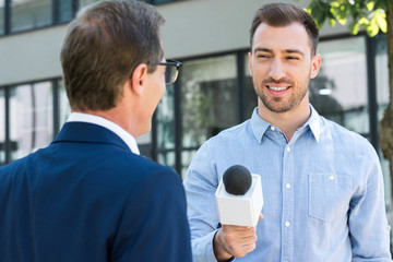 professional news reporter interviewing successful businessman with microphone