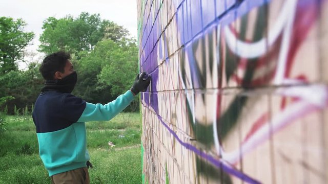 Young man graffiti artist painting on the wall, exterior