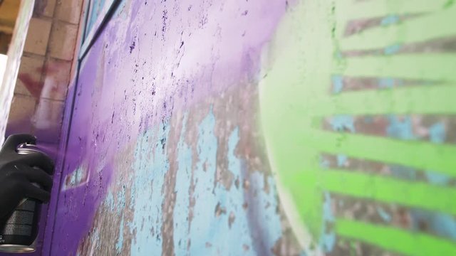 Young man graffiti artist painting on the wall, close up, slow motion