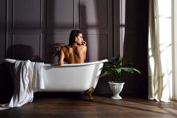 Young beautiful woman sitting in bathroom near expensive bathtub bath looking at the corner on dark 