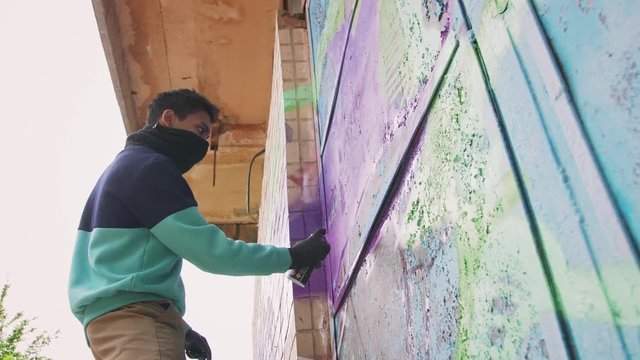 Young man graffiti artist painting on the wall, exterior