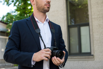 cropped view of photojournalist in formal wear with digital photo camera