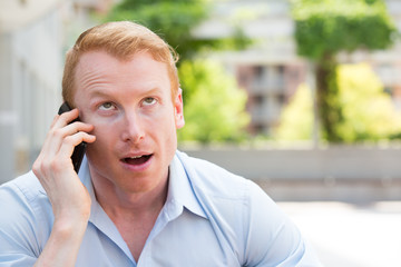 Closeup portrait, young man annoyed, frustrated, pissed off by someone talking on his mobile phone, bad news, isolated outdoors outside background. Long wait times, horrible conversations concept