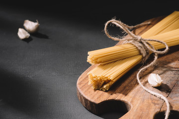 close-up shot of tied spaghetti with garlic on wooden cutting board and on black surface