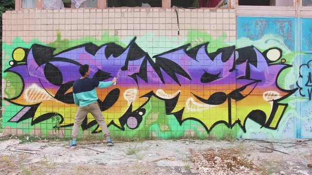 Young man graffiti artist painting on the wall, exterior