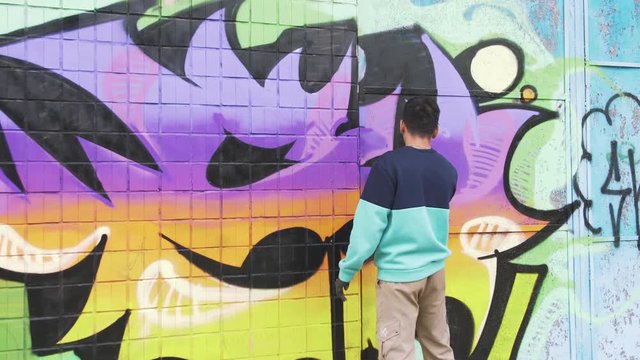 Young man graffiti artist painting on the wall, exterior