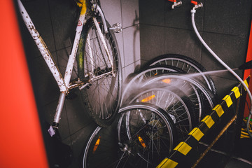 Services professional washing of bicycle in the workshop. Close-up of hand Young Caucasian stylish man doing bicycle cleaning using an automatic electric water pump. Sprays scatter from the pressure