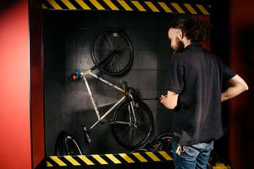 Fototapeta na wymiar Services professional washing of a bicycle in the workshop. Close-up of hand Young Caucasian stylish man doing bicycle cleaning using automatic electric water pump. Sprays scatter from the pressure
