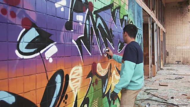 Young man graffiti artist painting on the wall, slow motion