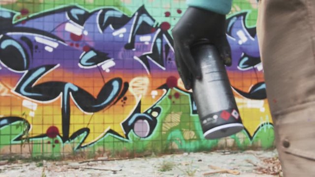 Graffiti artist with can on graffiti wall background, slow motion, close up