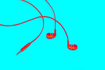 Red neon ear plugs on a teal background. Headphones for listening to music and sound on portable devices and jack for connection on a black background. Creative color