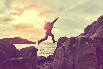 Jumping man hiker over a gap between two rocks