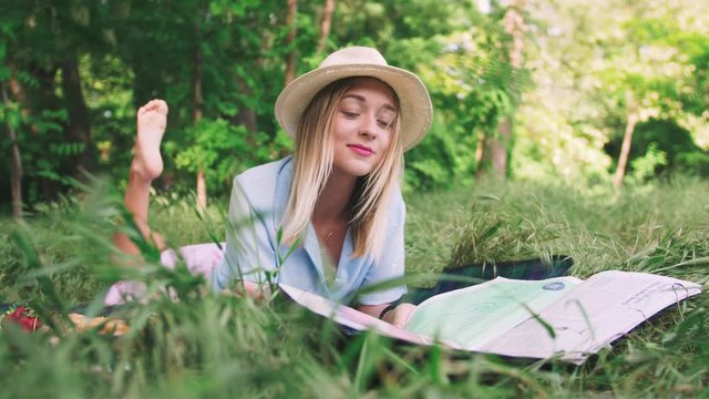 Portrait of happy romantic young woman in hat reading magazine outdoors in park on picnic