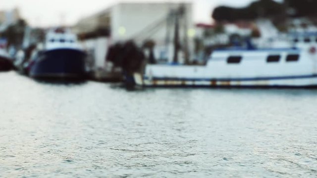 Water slowly flowing at a sunset in a sea port with boats on background.