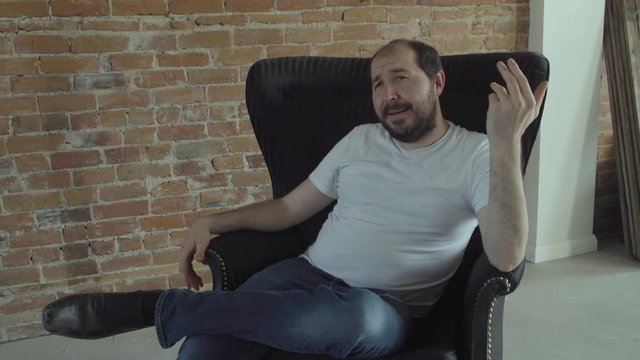 A self-confident man tells a story while sitting in an arm-chair.
