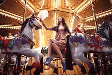 Fototapeta na wymiar Young beauty model woman posing with old horse carousel in summer park with magic lights