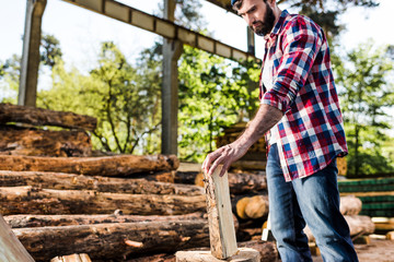 lumberjack in checkered shirt preparing to chop half of log at sawmill