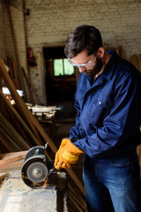 craftsman in protective googles and gloves using grinding machine at sawmill