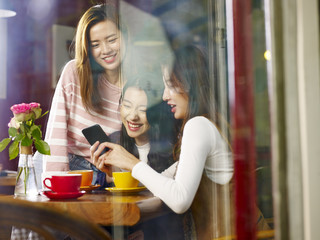 three young asian women looking at mobile phone in coffee shop