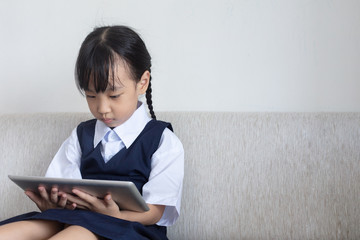 Asian Chinese little girl sitting on the sofa playing digital tablet