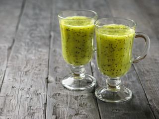 Two glasses of freshly made kiwi with cucumber smoothies on a black wooden table.